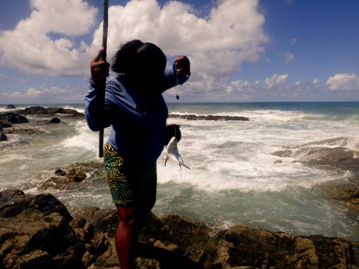 woman standing on rocks near ocean while fishing