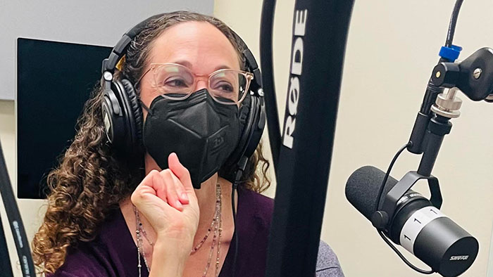 Pam Lach in front of audio equipment and a podcast microphone.