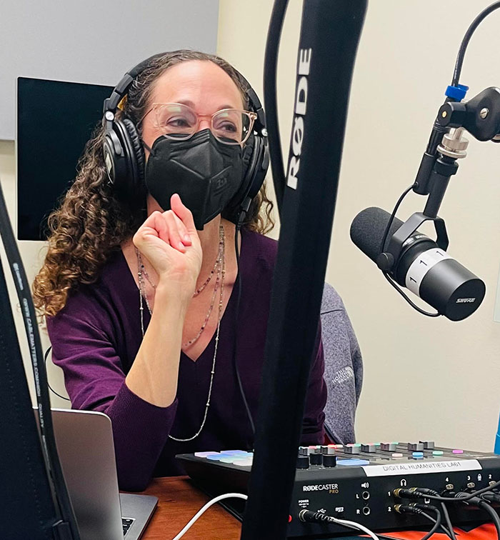 Pam Lach in front of audio equipment and a podcast microphone.