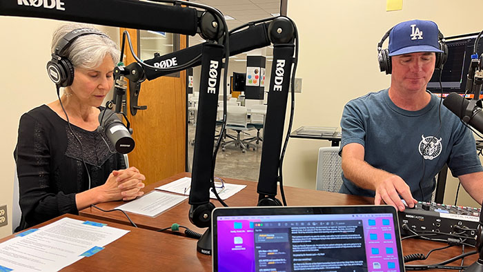 Two people in a recording studio with microphones, headphones, and audio equipment.