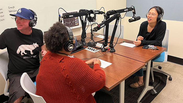 Three people recording a podcast in the DH studio with microphones, headphones, and a mixing board on the table.